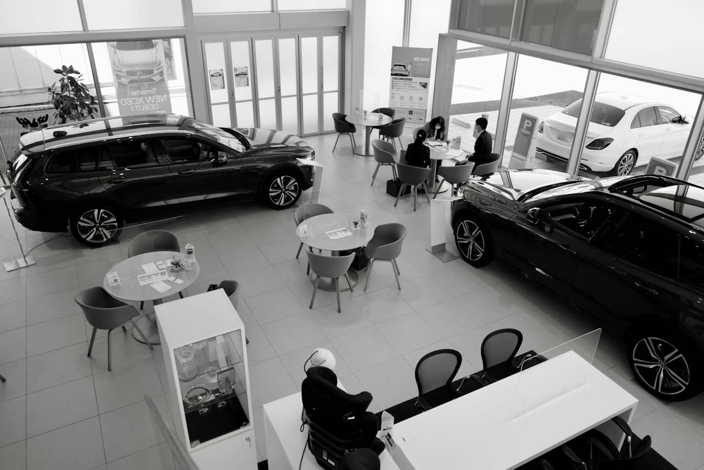 Customers discuss papers at tables in a modern car dealership showroom.