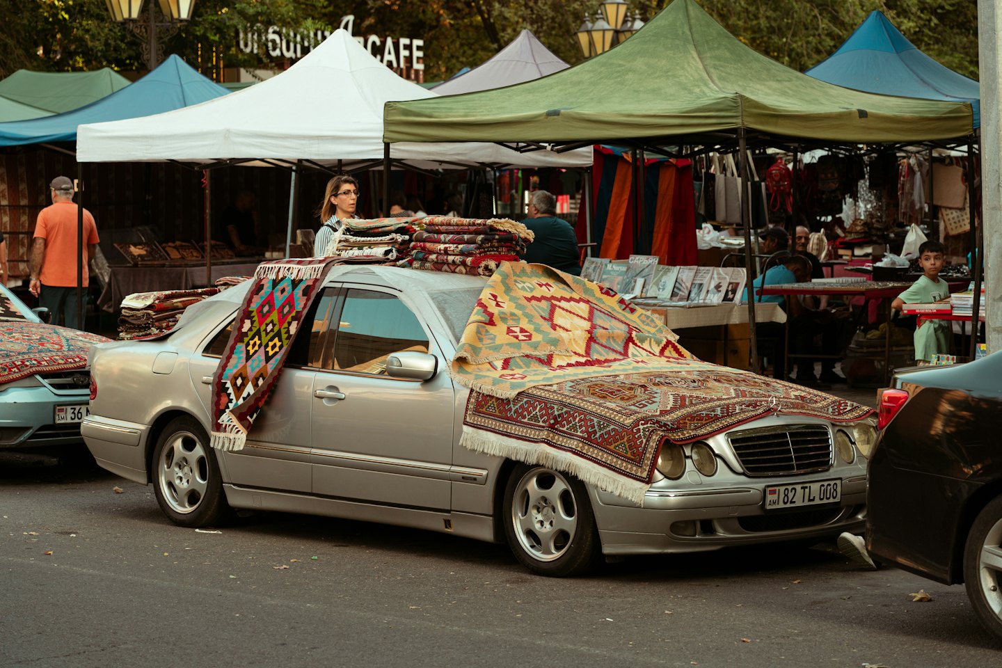 Patterned rugs displayed on a silver car at a street market.