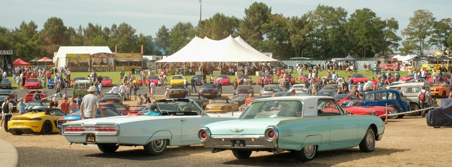 Visitors admire vintage cars parked at an outdoor show.