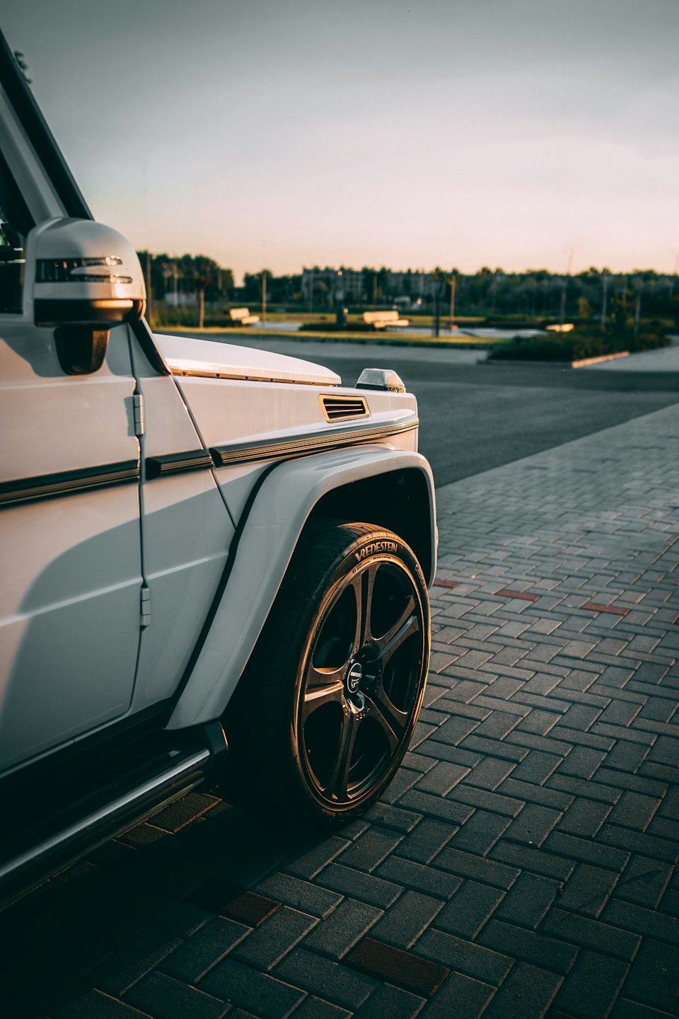 A white luxury SUV parked on pavers in golden hour light.